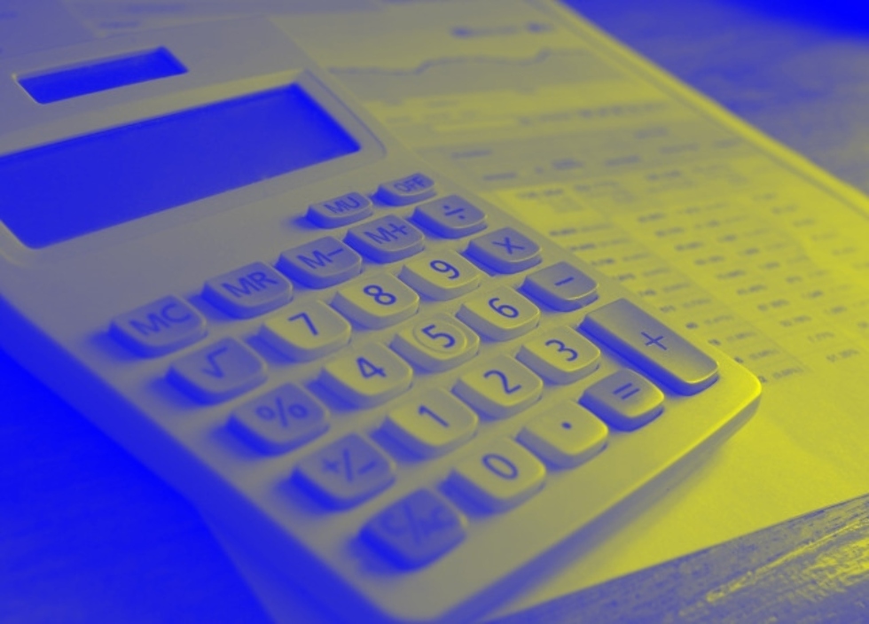 Yellow-and-blue-tinted monochrome photo showing a basic electronic calculator with a printed page of financial information on a desk